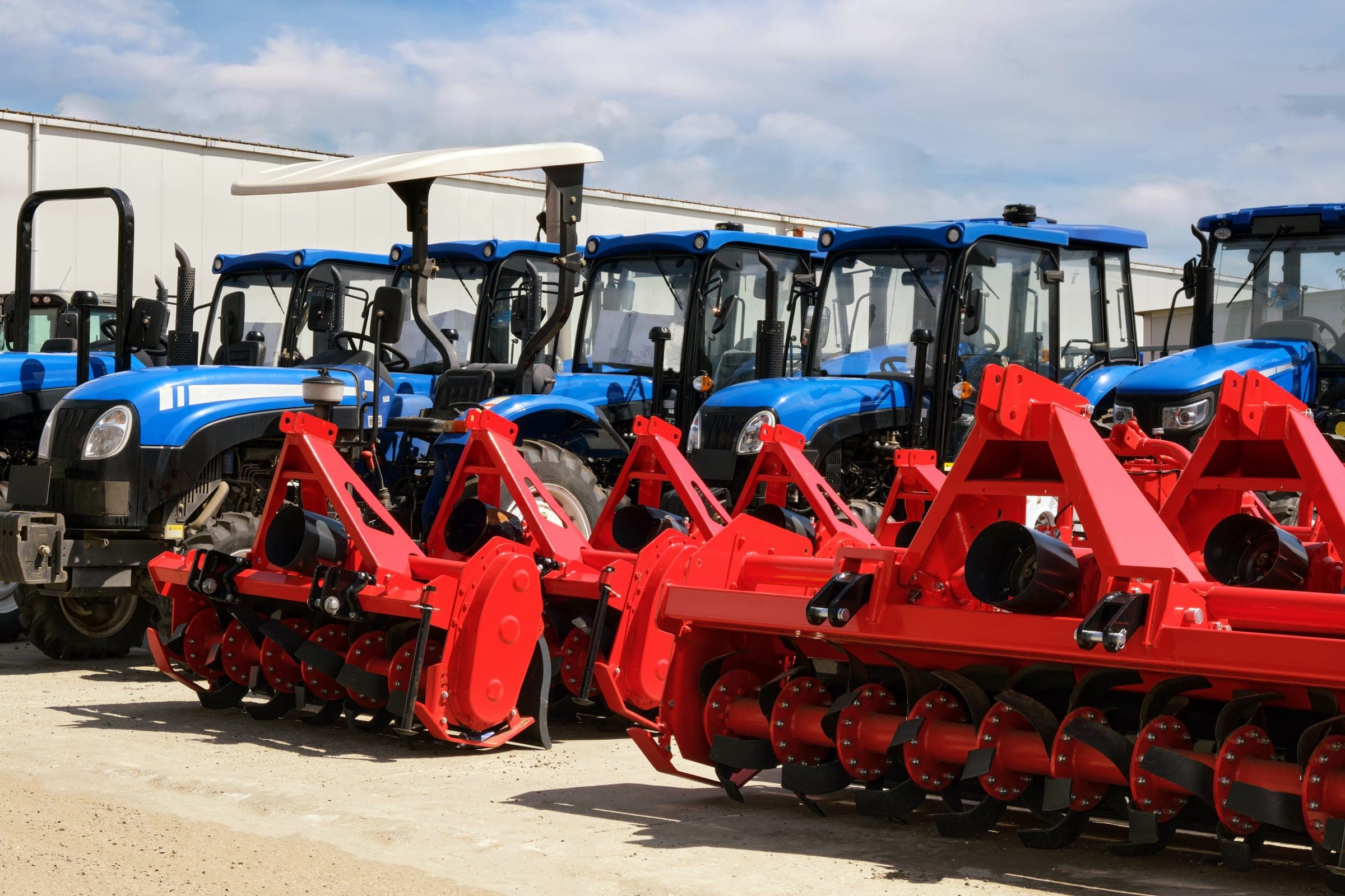 Row of blue tractors with red rotary tillers parked outdoors
