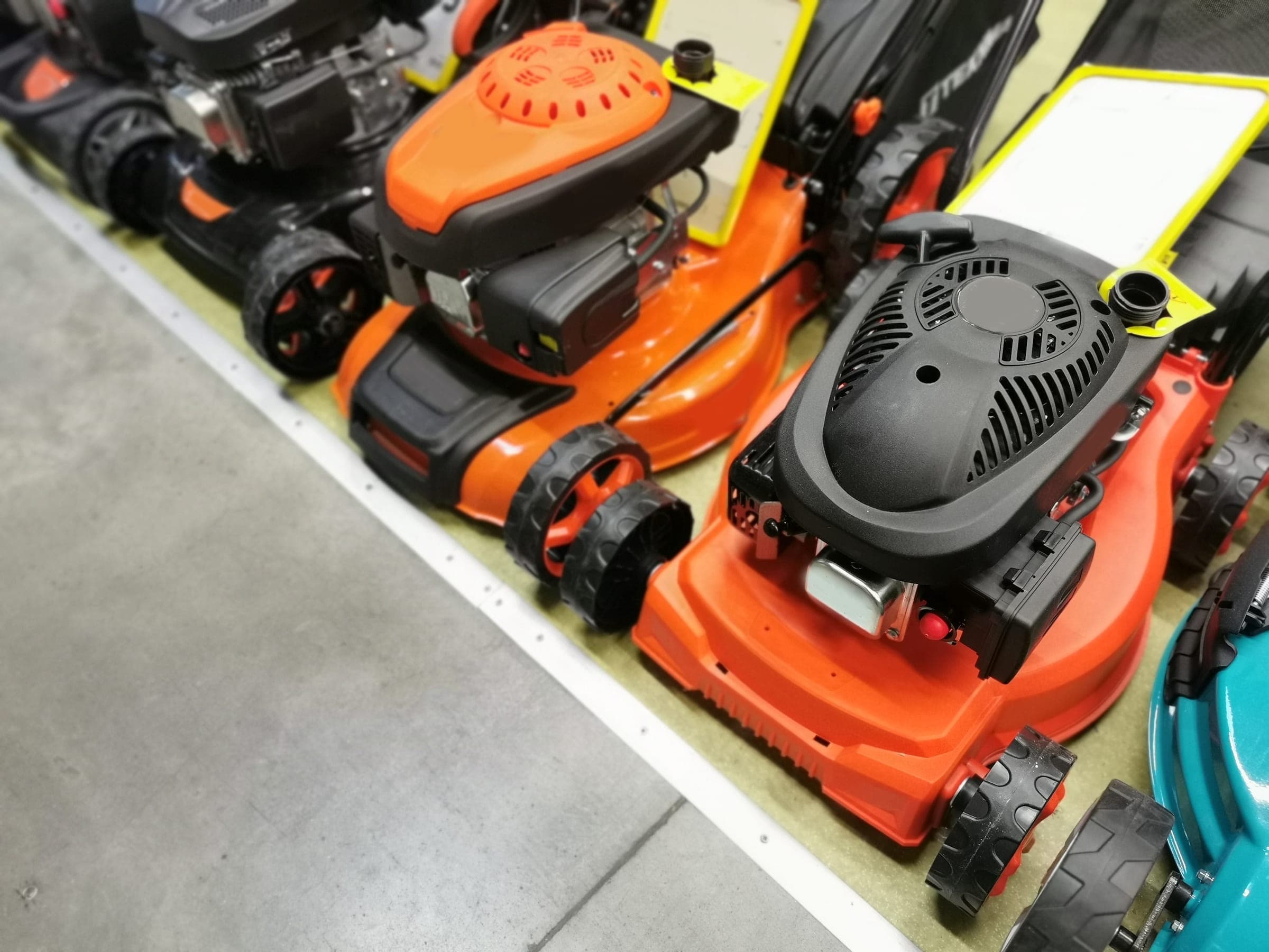 Orange petrol lawn mowers on a shop floor
